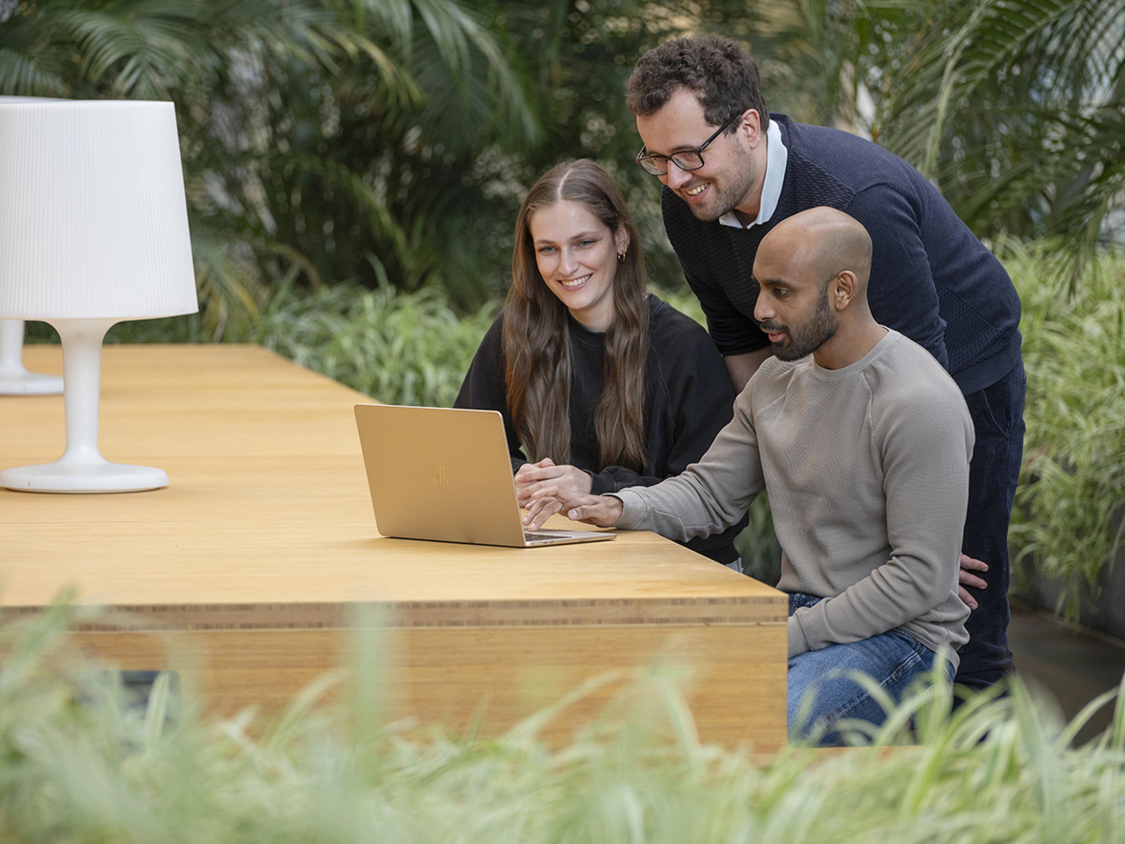 A woman and two man looking together at a laptop on a table, laughing.