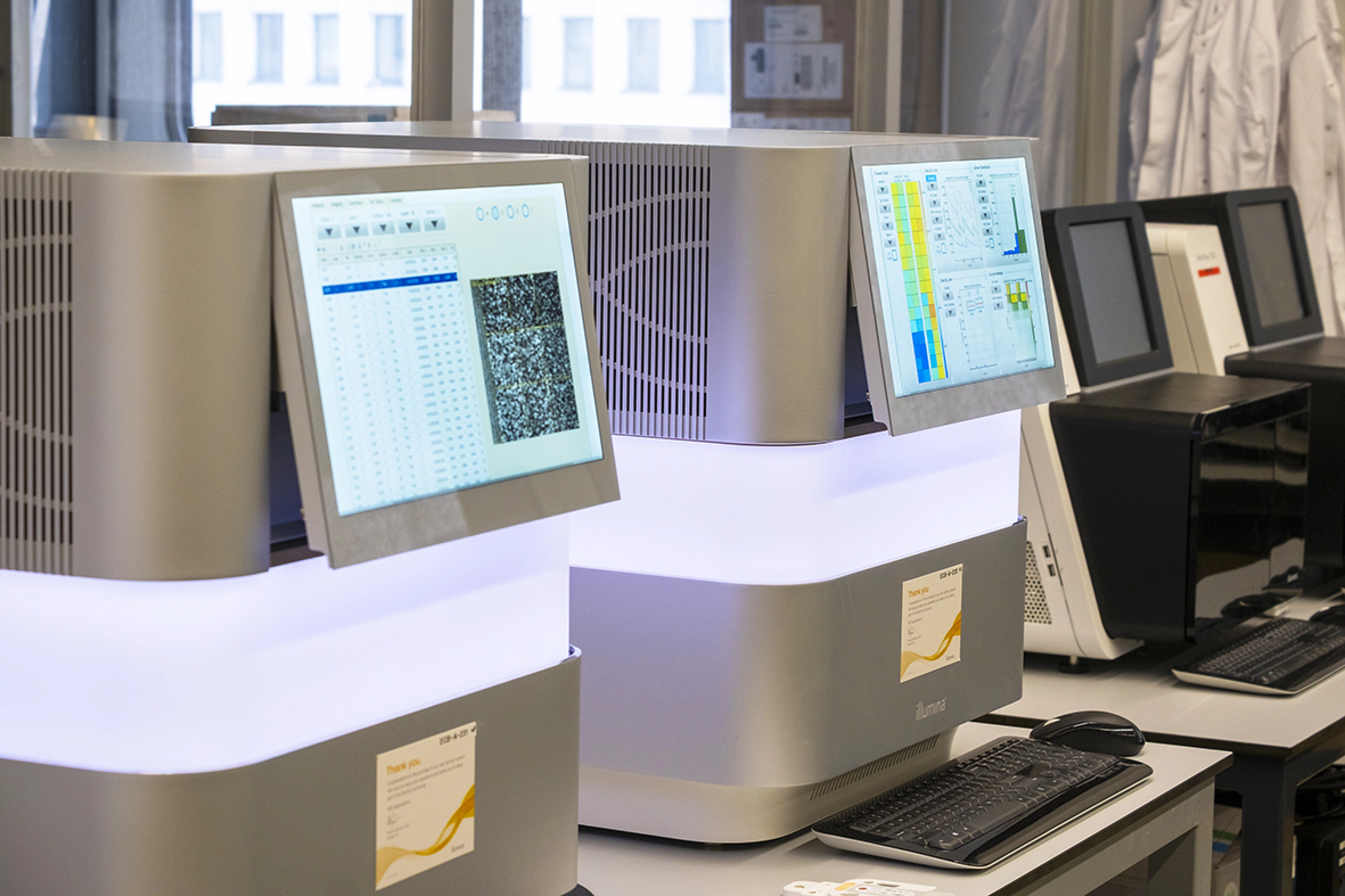 Two sequencers in a laboratory setting seen from the left front side, with white lights.