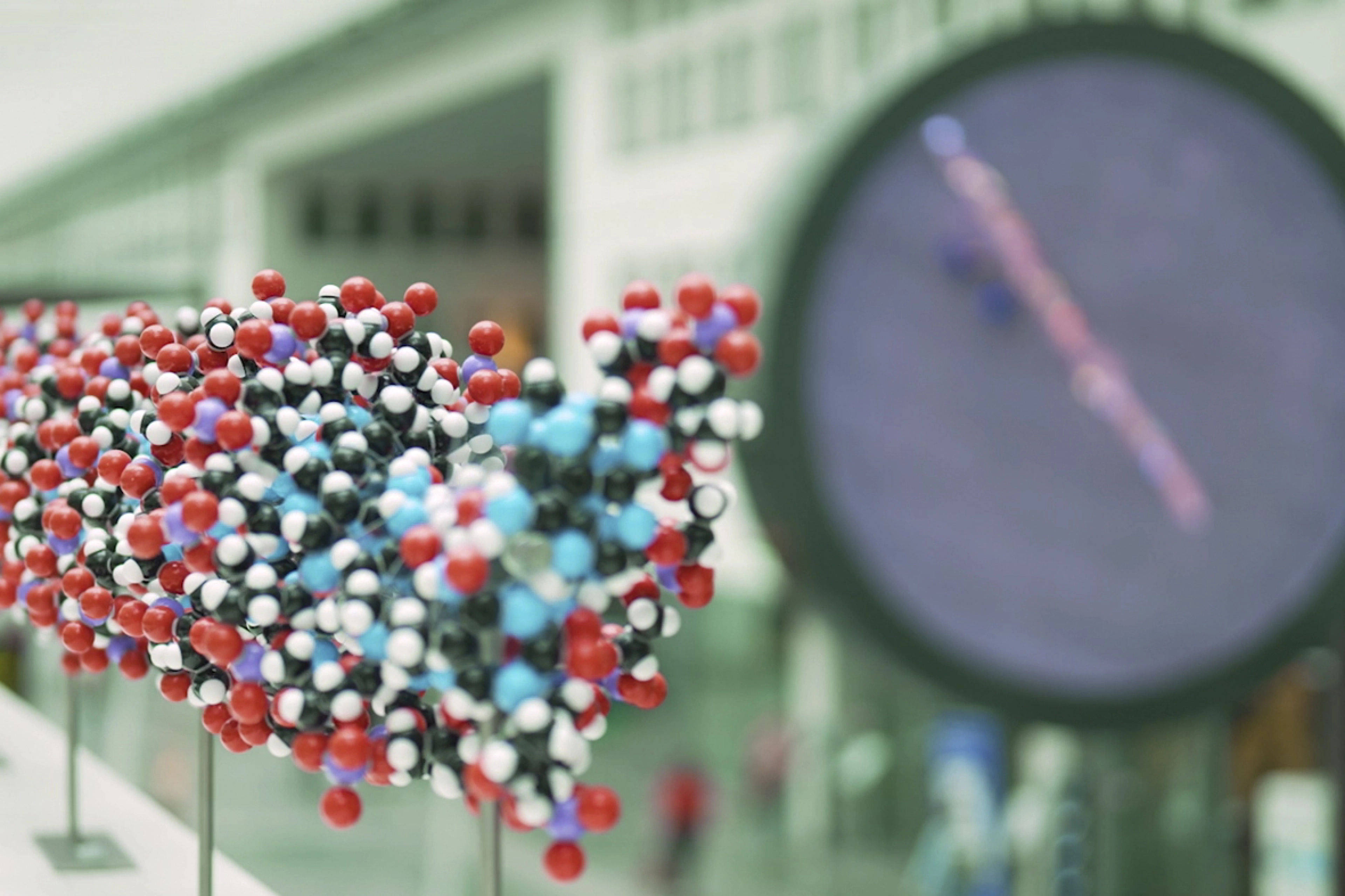 Close-up of the DNA molecule in redm white, blue black and purple with faded Erasmus MC clock in the hall in the background.